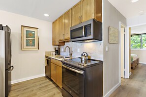 A modern kitchen with wooden cabinets, stainless steel appliances, and a built-in oven. - Elegant Island-Inspired 2-Bedroom with Ocean Views (Lahaina)