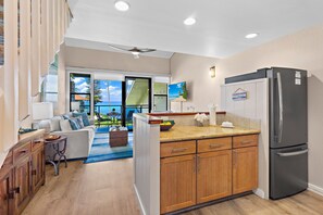 A modern kitchen with wooden cabinets, a stainless steel refrigerator, and a view to the outside.