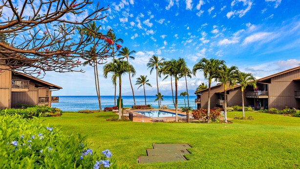 A resort with a pool, palm trees, and ocean views. - Elegant Island-Inspired 2-Bedroom with Ocean Views (Lahaina)