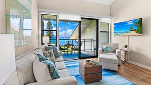 A living room with a sofa, coffee table, and a painting of a beach scene. - Elegant Island-Inspired 2-Bedroom with Ocean Views (Lahaina)