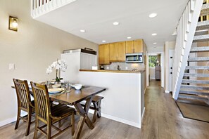 A modern kitchen with wooden cabinets, a central island, and a staircase leading to an upper level. - Elegant Island-Inspired 2-Bedroom with Ocean Views (Lahaina)