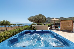 A hot tub with a view of the sea, outdoor furniture, and a wooden pergola.