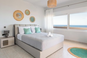 A bedroom with a bed, nightstand, lamp, and a view of the sea.