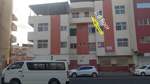 Un edifici de diverses plantes amb façana vermella i blanca, amb un rètol visible per 'AGRO-CENTRO' a la planta baixa, i una furgoneta blanca aparcada al davant.