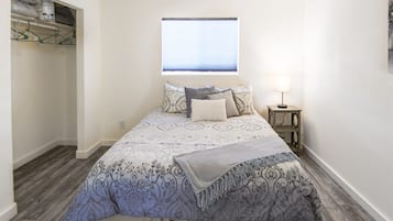 Een slaapkamer met een bed, nachtkastje, raam en kast.