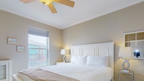 A hotel room with a large bed, a ceiling fan, a window with a view, two bedside tables with lamps, and a small side table with a lamp. - Close to the Beach, Shared Heated Pool, Boardwalk to the beach (Port Aransas)