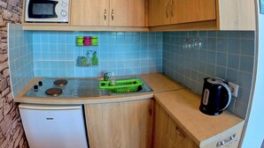 A compact kitchen with wooden cabinets, a microwave, a small refrigerator, a sink, and a kettle. - Beach Shack Studio s&l (Rhodes)