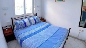A bedroom with a bed, a nightstand, a window, and a wall-mounted picture. - Deluxe Beach Apartment- Sleeps 2 & Private Terrace (Rhodes)