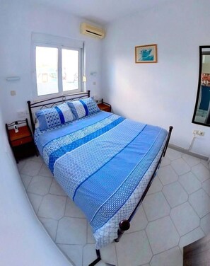 A bedroom with a bed, a window, an air conditioning unit, a framed picture, and a tiled floor. - Deluxe Beach Apartment- Sleeps 2 & Private Terrace (Rhodes)