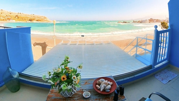 A balcony with a view of the beach, a table with flowers, and two chairs. - Deluxe Beach Apartment- Sleeps 2 & Private Terrace (Rhodes)