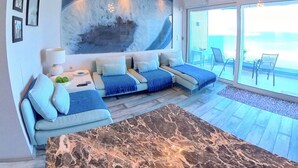 A modern living room with a sectional sofa, a marble coffee table, and a large window offering a view of the ocean. - Deluxe Beach Apartment- Sleeps 2 & Private Terrace (Rhodes)