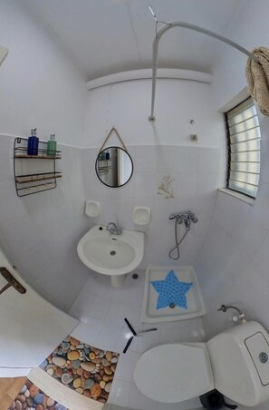 A bathroom with a sink, mirror, shower, and a small window.