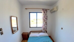 Ein kleines, sauberes Zimmer mit einem Bett, einem Fenster mit Vorhängen, einer Pendelleuchte und einer Klimaanlage.