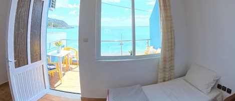 Ein Schlafzimmer mit Bett, einem Fenster mit Meerblick und einer Tür zu einem Außenbereich mit Tisch und Stühlen.