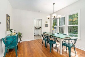 Een eethoek met een houten vloer, teal stoelen, een groene tafel, en een keuken op de achtergrond.