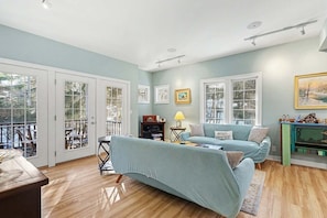 A living room with a sofa, a small table, and a lamp. There are two doors leading to a balcony.