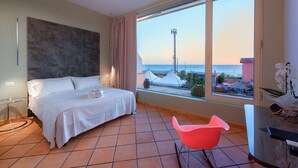 A hotel room with a bed, a glass table, a pink chair, and a view of the sea. - La Risacca Relais  (Belvedere Marittimo)