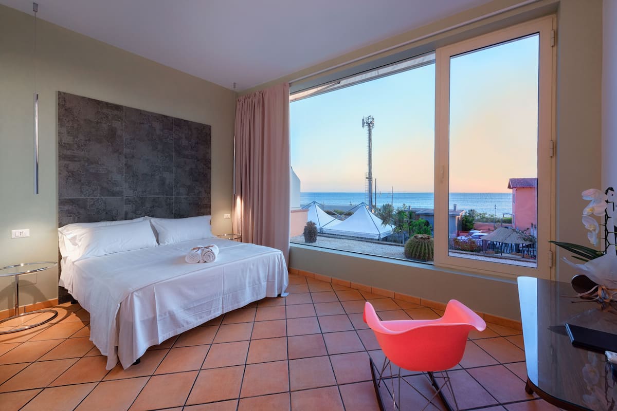 Habitación de hotel con cama, una mesa de vidrio, una silla rosa y vista al mar.