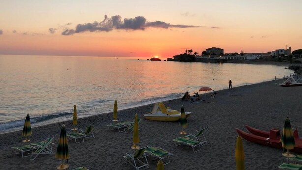 A beach with sun loungers and umbrellas, a calm sea, and buildings in the background. - La Risacca Relais  (Belvedere Marittimo)