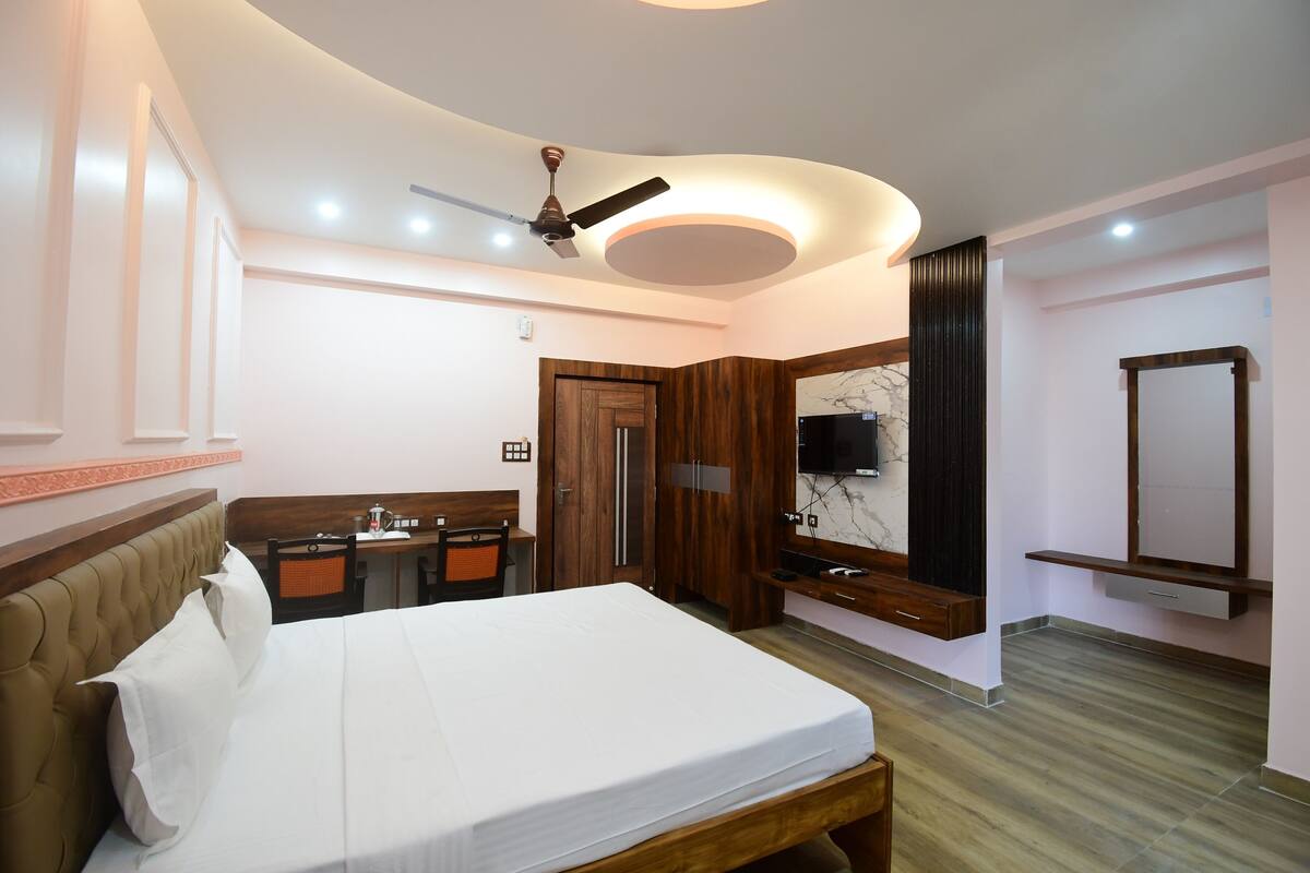 A bedroom with a bed, a desk, a chair, a wardrobe, a ceiling fan, and a TV.