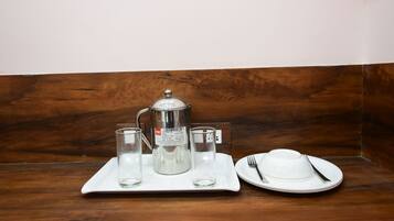 A tray with a coffee maker, two glasses, and a plate with a fork and knife on a wooden table.
