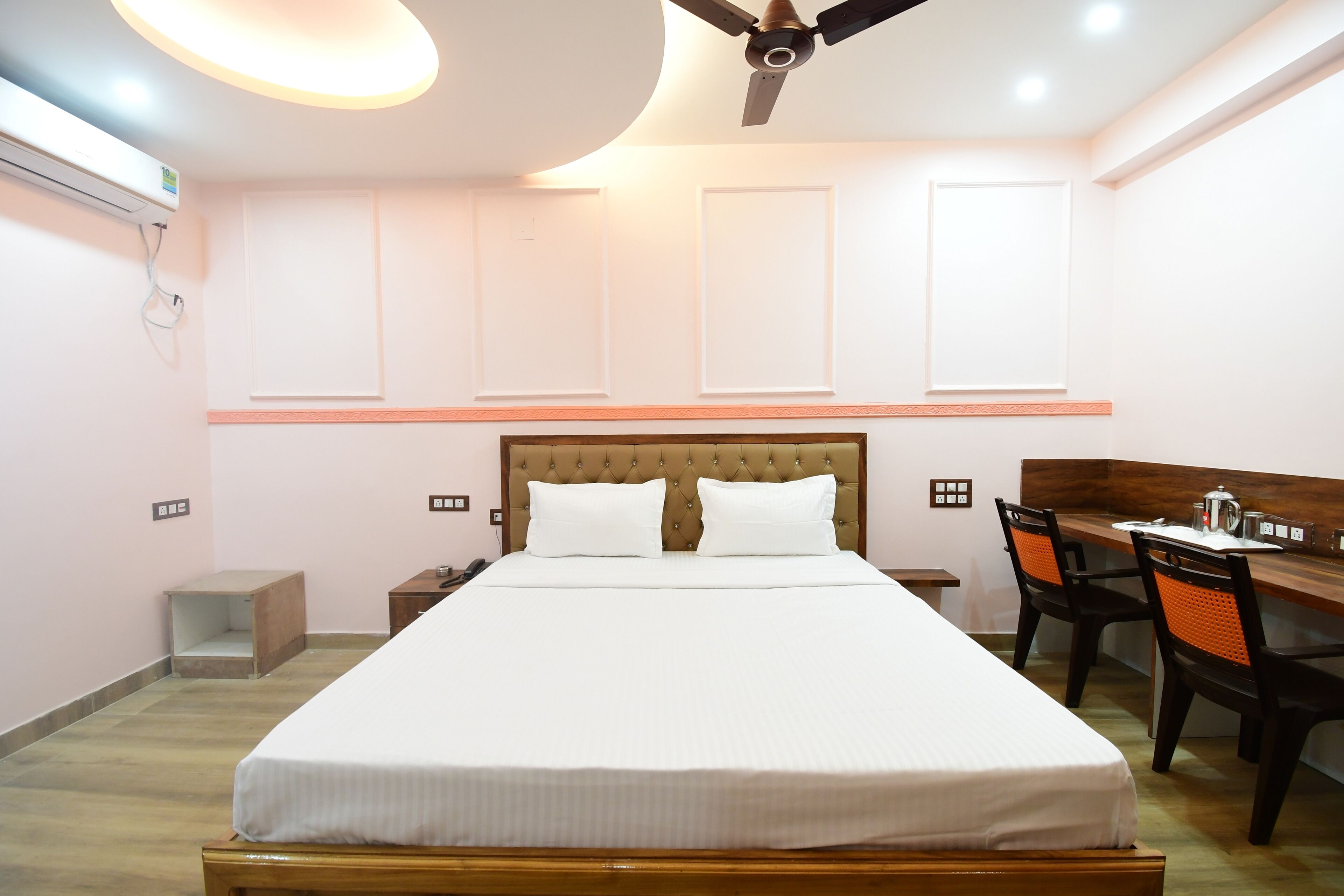 A hotel room with a large bed, a desk, and a chair. There is a ceiling fan, a nightstand, and a small table.
