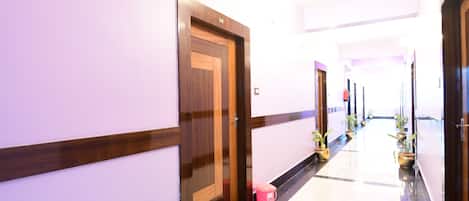 A hallway with wooden doors, potted plants, and a tiled floor.