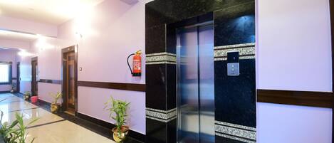 A modern hotel lobby with a marble floor, a reception desk, and an elevator.
