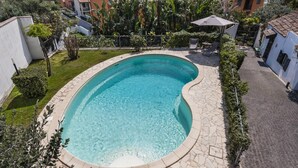 Piscina com borda curva, rodeada por um terraço pavimentado e um pequeno jardim.