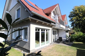 A two-story house with a balcony, large windows, and a small patio area.