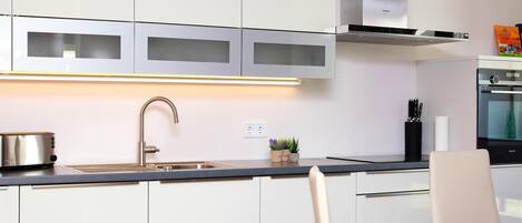 Una cocina moderna con gabinetes blancos, una campana de acero inoxidable y un horno empotrado.