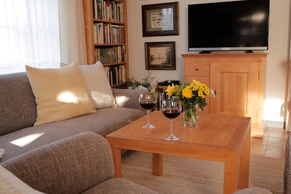 A living room with a sofa, a coffee table with wine glasses, a bookshelf, a flat-screen TV, and a wooden cabinet.