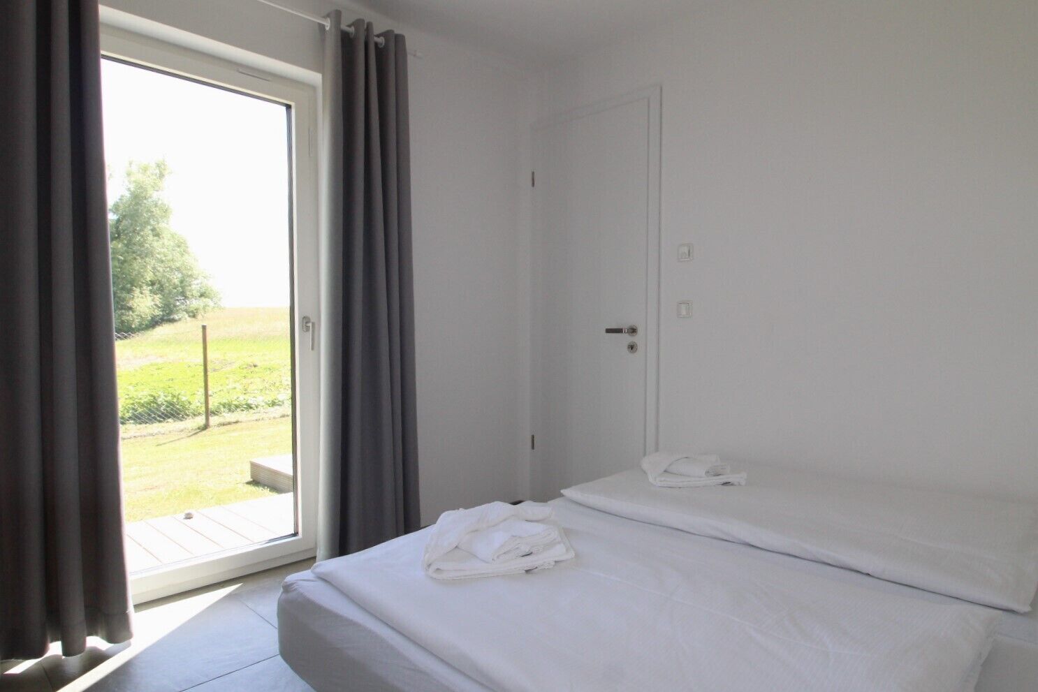 Ein Hotelzimmer mit einem Bett, einer Tür und einem mit Vorhängen versehenen Fenster.