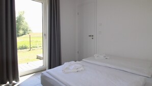 A hotel room with a bed, a door, and a window with curtains. - Freistehender Bungalow in der Künstlerkolonie Ahrenshoop (Ostseebad Ahrenshoop)