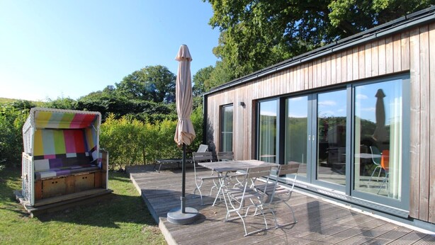 A modern house with a wooden deck, outdoor furniture, and a colorful fabric structure. - Freistehender Bungalow in der Künstlerkolonie Ahrenshoop (Ostseebad Ahrenshoop)