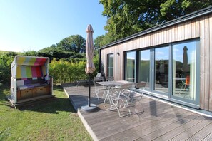 Une maison moderne dotée d’une terrasse en bois, de mobilier d’extérieur et d’une structure en tissu aux couleurs vives.
