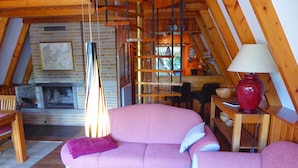 A cozy loft-style room with a fireplace, a pink sofa, wooden furniture, and a red lamp.