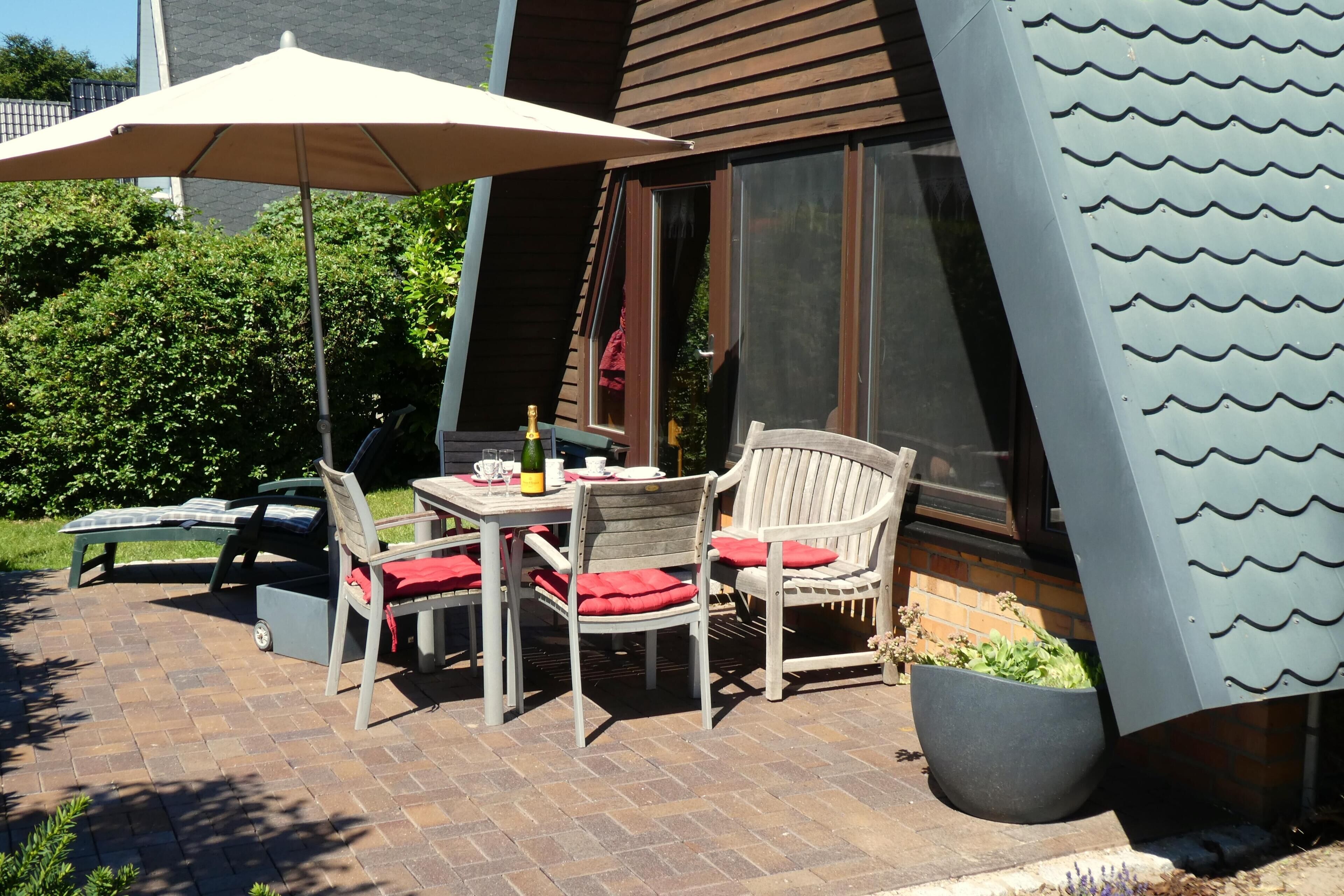 Un patio al aire libre con una mesa, sillas, una planta en maceta y un paraguas grande.