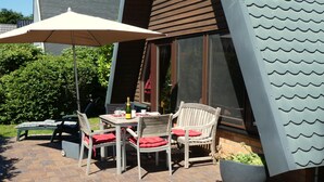 An outdoor patio with a table and chairs, a potted plant, and a large umbrella.