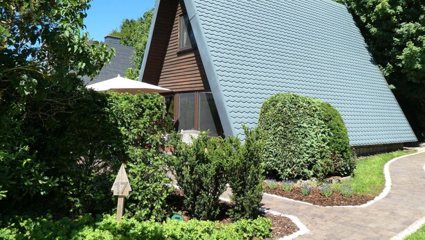 A house with a unique sloped roof, surrounded by greenery and a paved driveway.