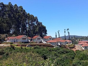 A row of white buildings with red roofs, surrounded by greenery and trees.