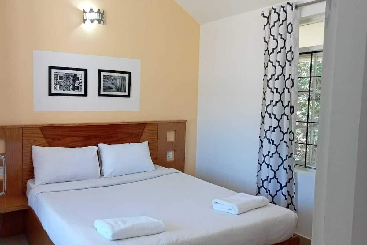 Een hotelkamer met een houten hoofdeinde, twee witte kussens, een netjes opgemaakt bed met witte lakens en twee ingelijste foto's aan de muur.