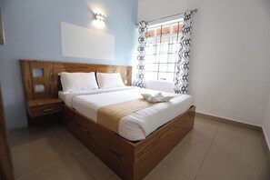 A neatly made bed in a room with a wooden headboard, a nightstand, and a window with patterned curtains.