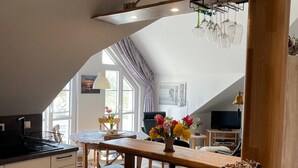 A modern kitchen with a central island, white cabinetry, and a dining area with a wooden table and chairs. - Künstlerkolonie Ahrenshoop (Ostseebad Ahrenshoop)
