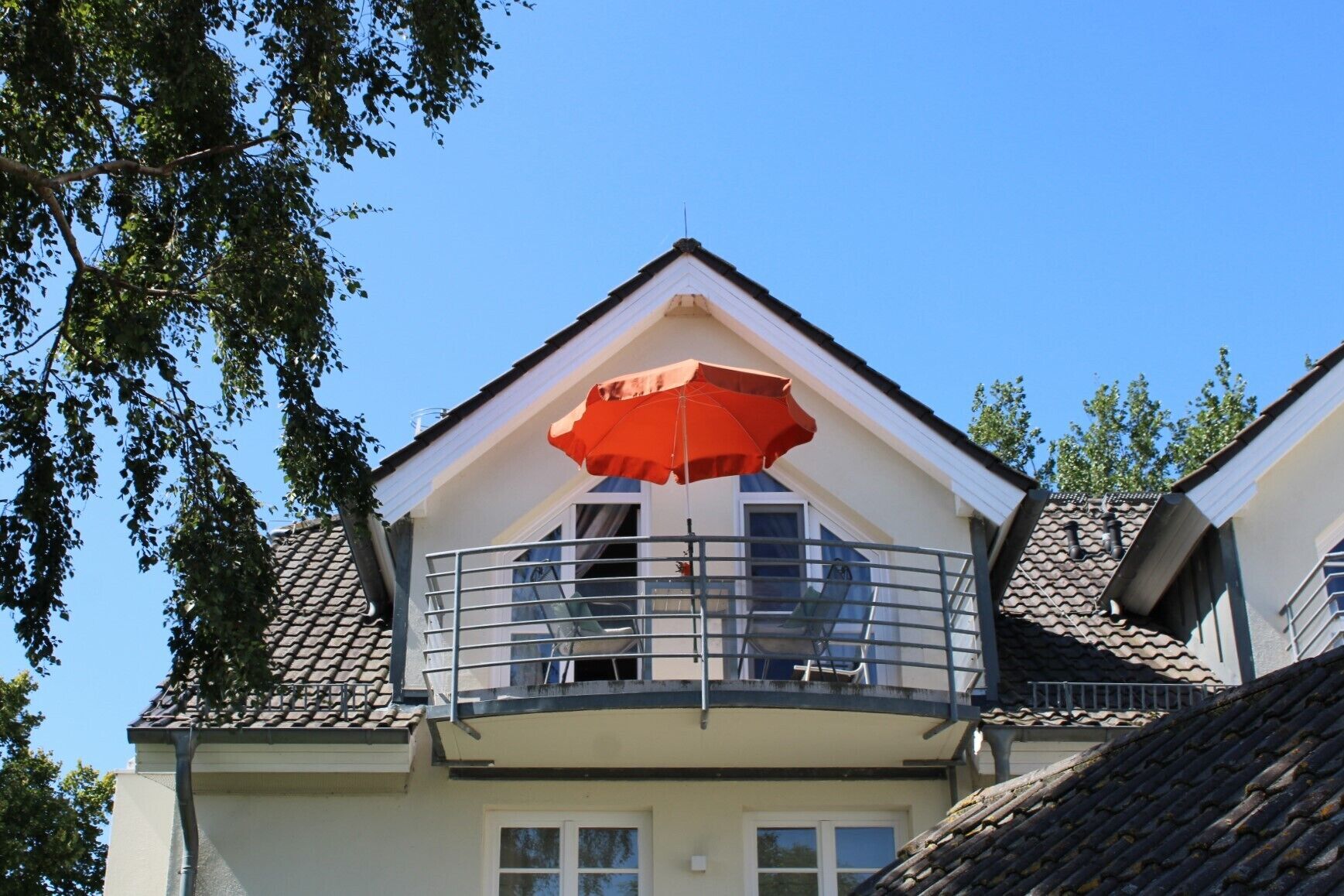 A residential building with a balcony featuring a metal railing and a red umbrella.