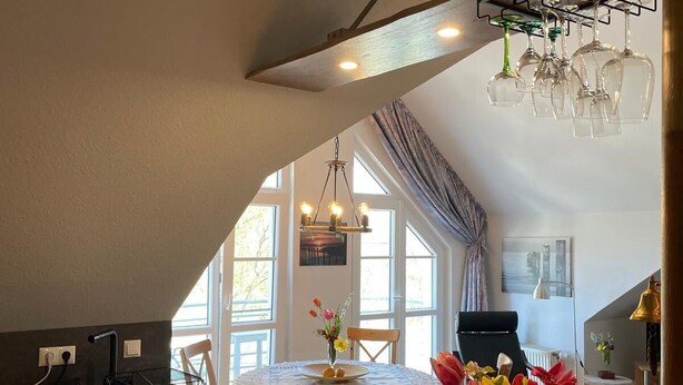 A kitchen with a dining area, featuring a wooden table, chairs, and a vase of flowers. - Künstlerkolonie Ahrenshoop (Ostseebad Ahrenshoop)
