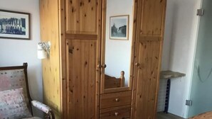 A bedroom with a wooden wardrobe, a bed, a sofa, and a small table. - Künstlerkolonie Ahrenshoop (Ostseebad Ahrenshoop)
