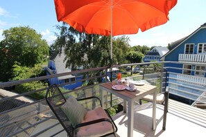Un balcon avec une table, des chaises et un parasol orange.