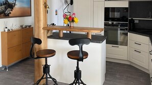 A modern kitchen with a wooden island, bar stools, and a hanging light fixture. - Künstlerkolonie Ahrenshoop (Ostseebad Ahrenshoop)