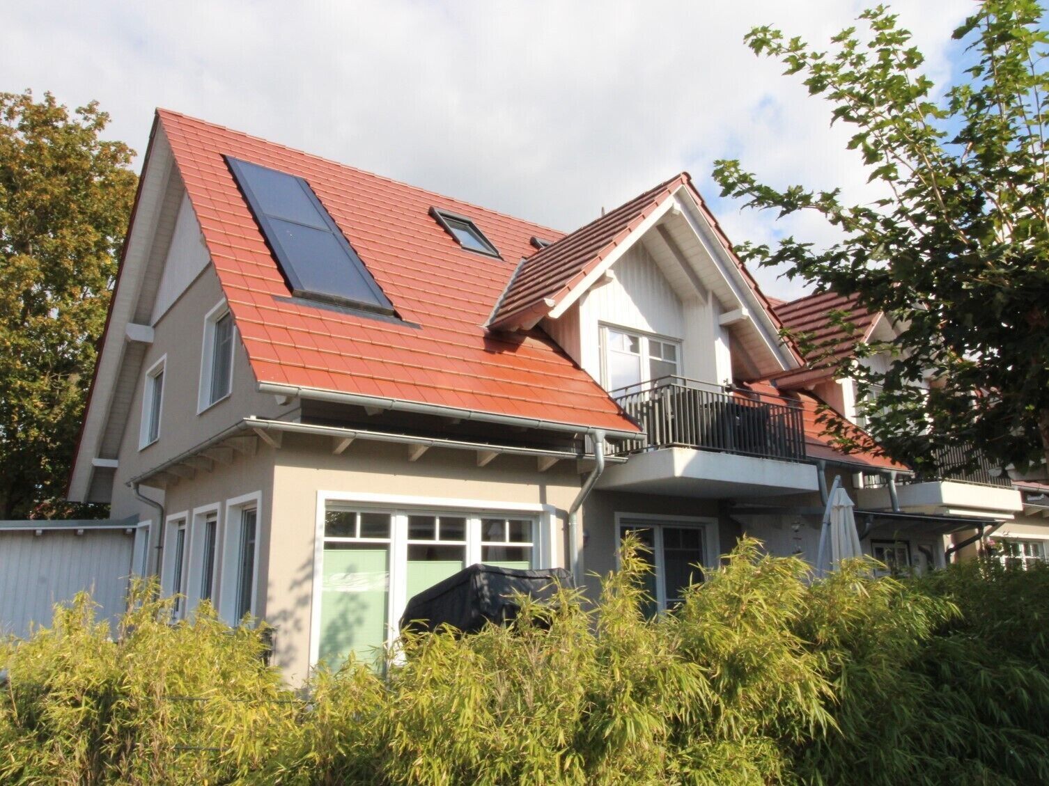 Een twee verdiepingen tellend huis met een rood dak, een balkon en een garage.